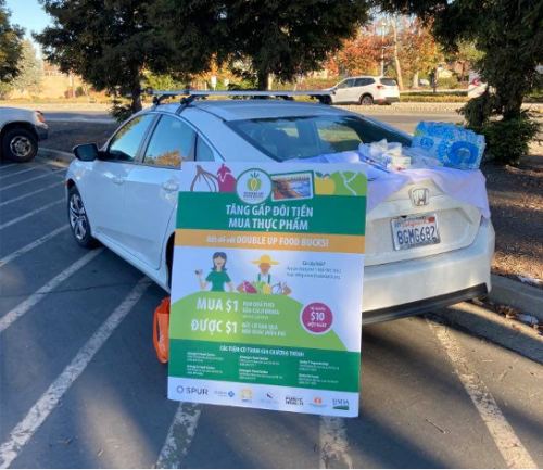A DUFB poster leans against the car of outreach staff from Second Harvest of Silicon Valley at a food distribution site in San Jose