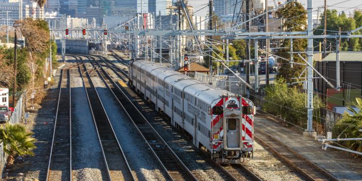 A train travels along a track surrounded by buildings and trees. 