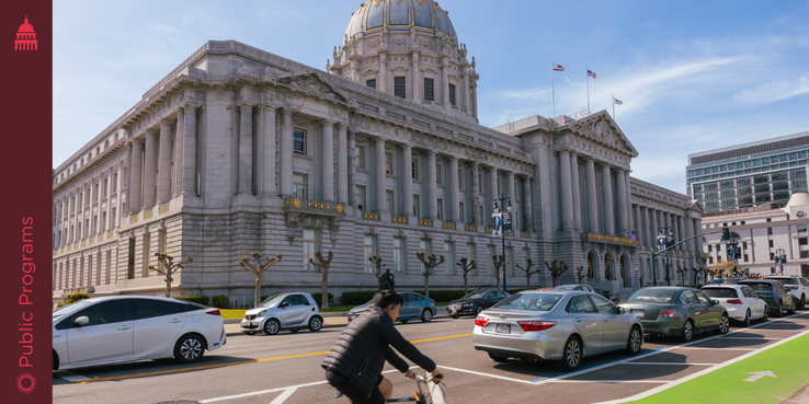 Image of cyclist passing parked cars in front of SF City Hall