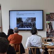 Group of participants from the SPUR study trip watch a presentation on car-free Copenhagen in a brightly lit room with wooden furniture and posters