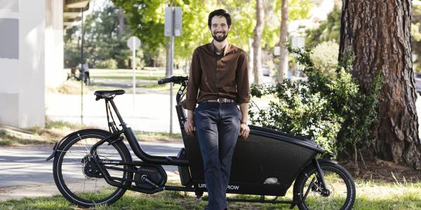 Outdoor photo of Eli Zigas standing in front of a large black bike