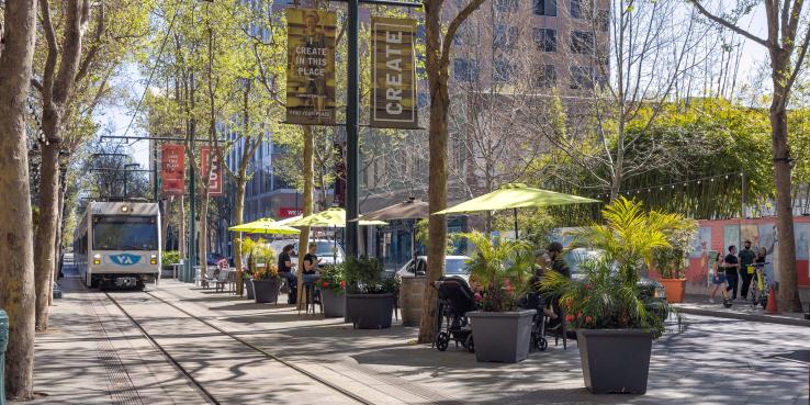 People sitting at cafe tables with umbrellas and potted plants on South First Street in San José