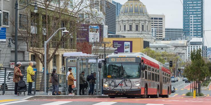 Photo of people boarding a Muni bus with San Francisco City Hall dome in the background