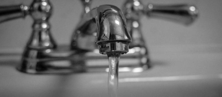 Black and white photo of a sink faucet running water