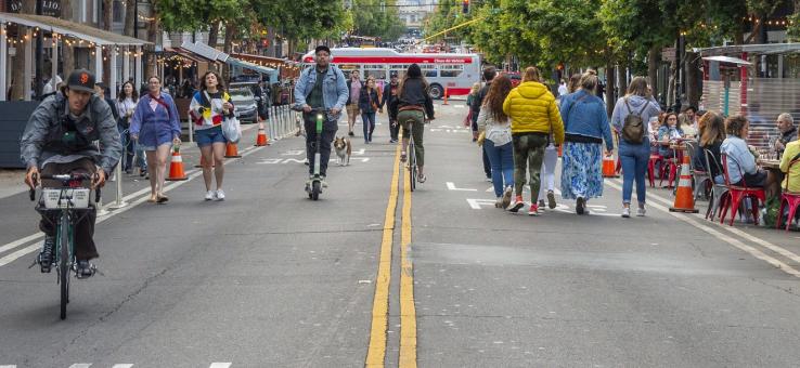 people biking, walking and eating at outdoor tables on a street closed to vehicles