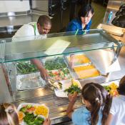 Cafeteria Worker Serving Trays of Healthy Food to Children
